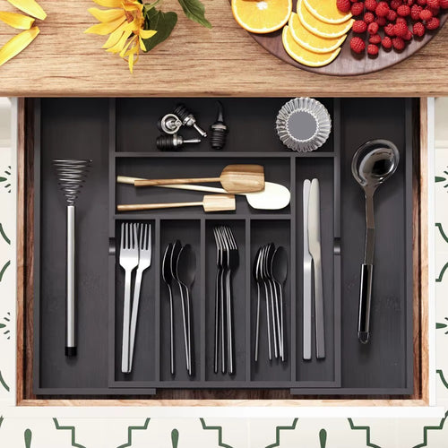 Expandable kitchen drawer organizer with compartments holding cutlery, utensils, whisk, ladle, and kitchen tools neatly arranged.