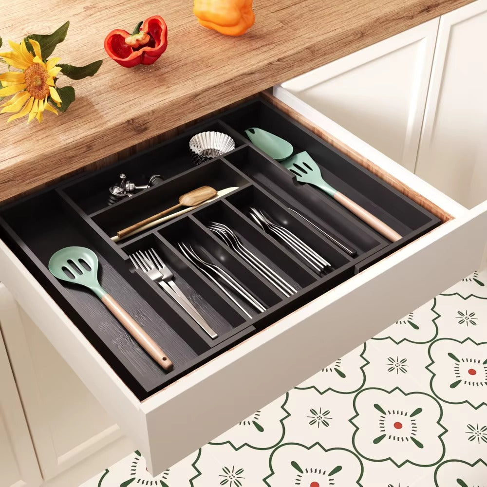 Black expandable drawer organizer in a kitchen drawer, holding cutlery, utensils, and kitchen tools neatly arranged.