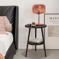 Black side table with a pink lamp next to a bed in a bedroom setting.