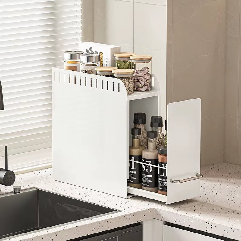 White pull-out kitchen organizer storing spice jars, sauces, and condiments on a countertop near the sink.