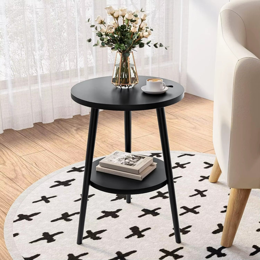 Black round side table with a vase of flowers and a cup on a white rug with black patterns, next to a beige armchair.