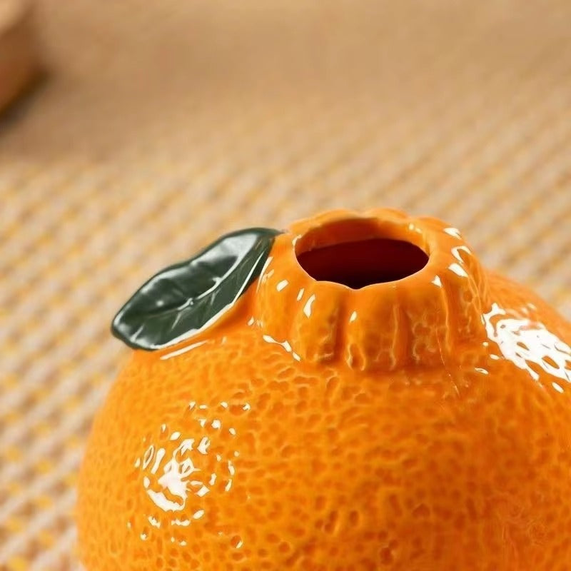 Close-up of a glossy orange-shaped ceramic vase showing detailed textured peel design and small leaf accent.