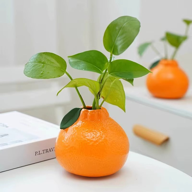 Small orange-shaped plant pot with green leaves, used as a decorative indoor planter on a tabletop.