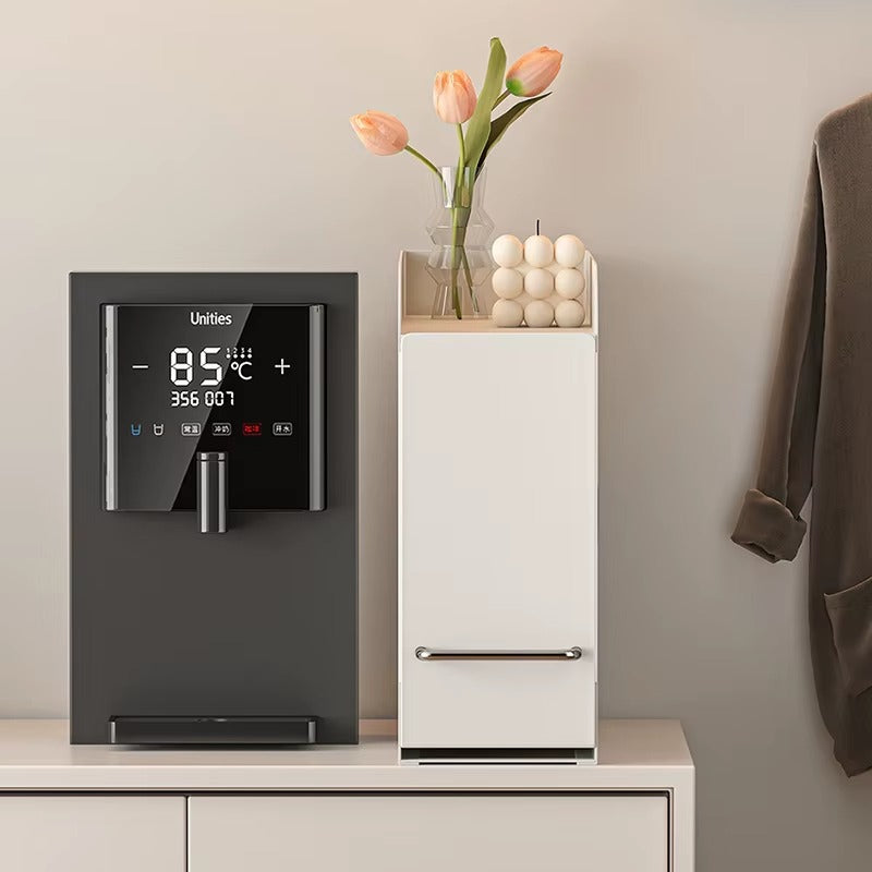 Slim pull-out storage cabinet used as a coffee station organizer, topped with a vase of flowers and decorative candles.